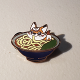 A picture of an enamel pin featuring a fox eating kitsune udon